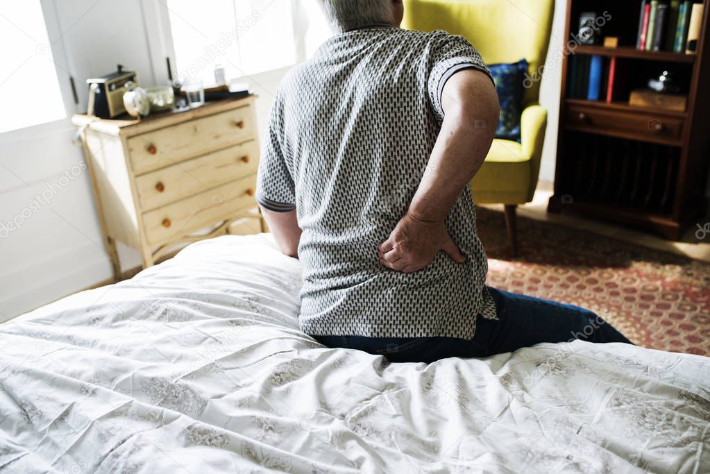 Senior man sitting on bed with pain in small of back 