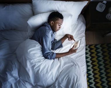 Karanlıkta bir dijital cihaz kullanarak yatakta adam