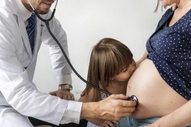 Daughter kissing pregnant mother's belly while doctor having monitoring belly   clipart
