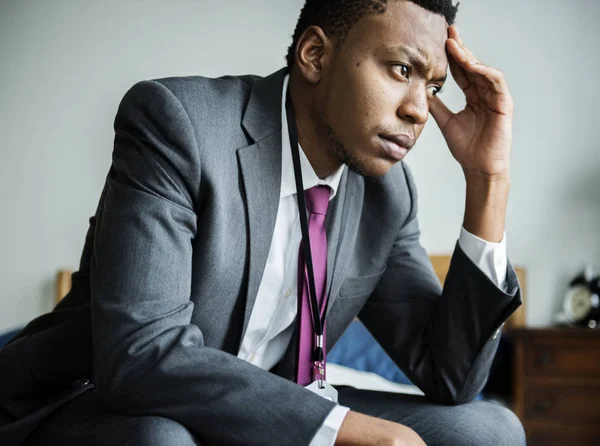 concerned african man in suit sitting on bed