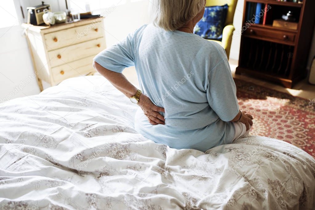 Senior woman sitting on the bed in pain in small of back