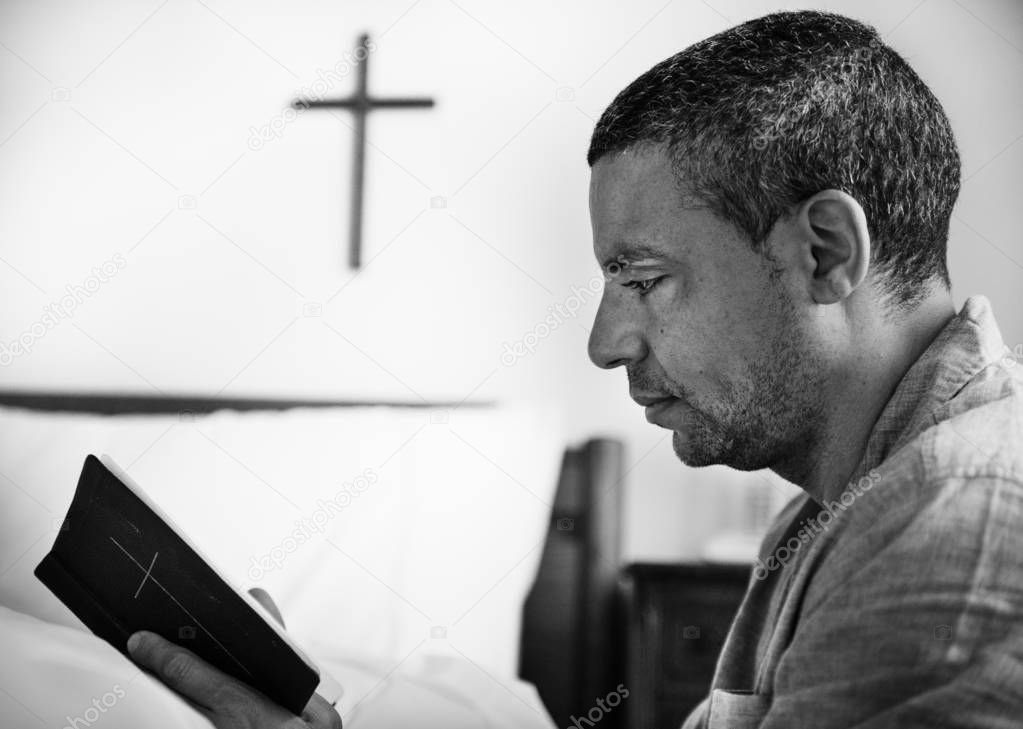 man reading a bible in bedroom, black and white