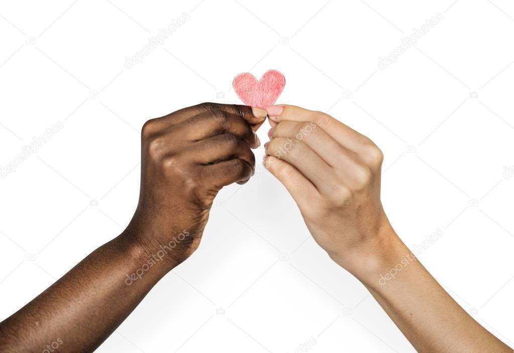 Hand of african human and hand of caucasian human holding heart together  