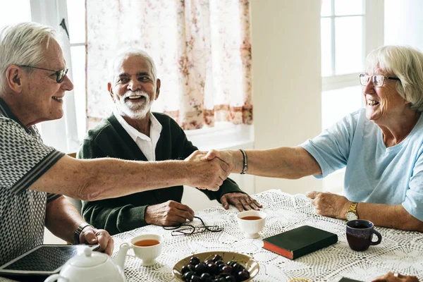 老人握手 坐在餐桌上喝茶在家 — 图库照片