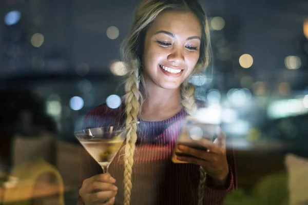Happy young woman using a smartphone at a rooftop bar in the evening