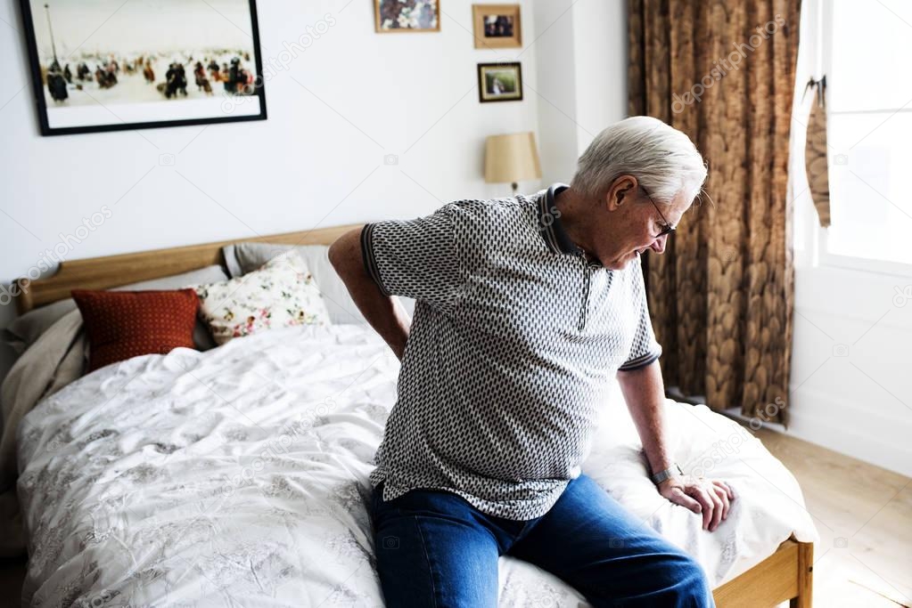 Senior man sitting on bed with pain in small of back 