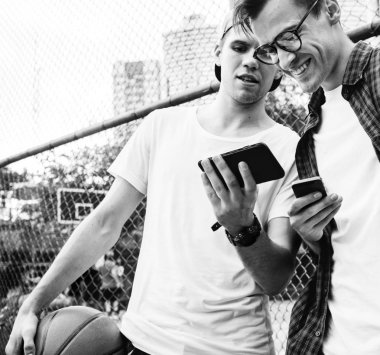 Genç yetişkin erkek arkadaşlar akıllı telefonlar millennials kavramı kullanarak basketbol sahasında