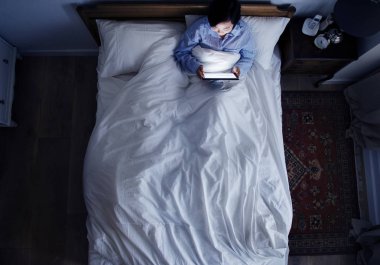 Karanlıkta bir dijital cihaz kullanarak yatakta kadın