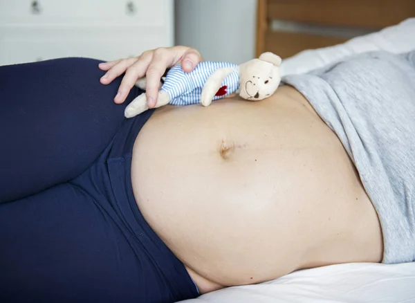 怀孕妇女睡在床上与泰迪熊在腹部 — 图库照片