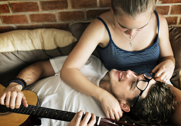Caucasian couple on the bed, man playing a guitar