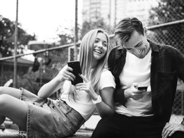 Mutlu sevimli genç çift parkta akıllı telefonlar birlikte, siyah ve beyaz kullanma