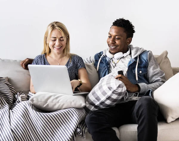 Cute interracial couple on a couch sharing laptop love, internet and music concept