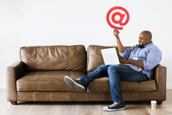 Homem Negro Relaxando Sofá Segurando Laptop Com Sinal Atmark — Fotografia de Stock