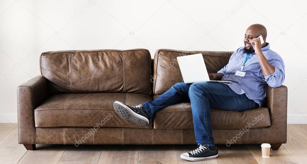 Black man relaxing on sofa and holding laptop