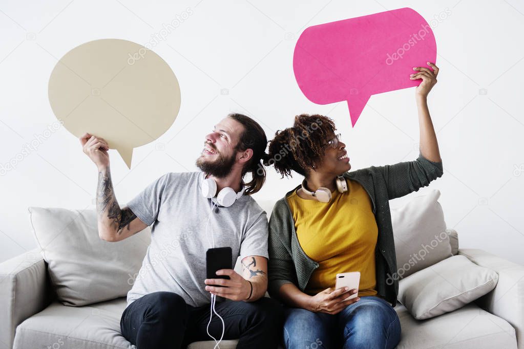 Interracial couple sharing music at home holding copyspace speech bubbles