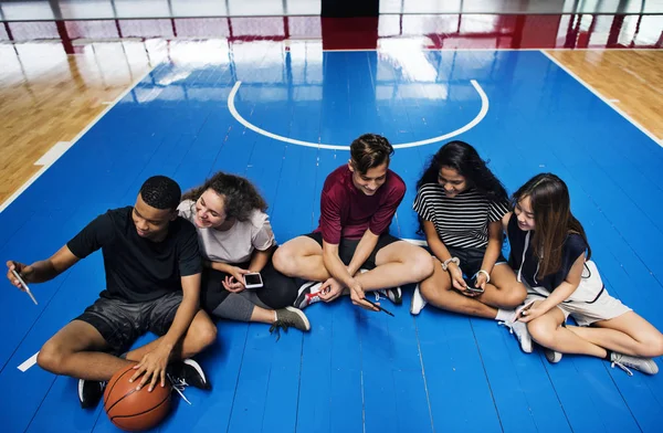 一群年轻的青少年朋友在一个篮球场放松和使用智能手机 — 图库照片