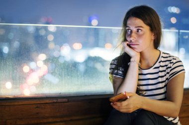Bir smartphone akşam cityscape tutan mutsuz genç kadın