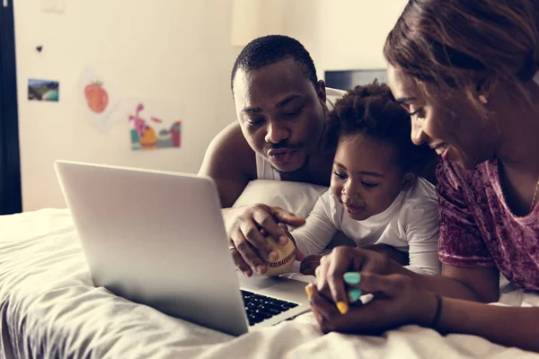 African family lying on bed using laptop together in bedroom