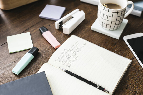 close-up shot of opened notebook with stationery and cup of coffee on wooden table