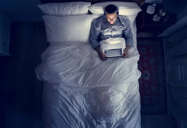 Człowiek Łóżku Przy Użyciu Jego Laptop Słuchawki — Zdjęcie stockowe