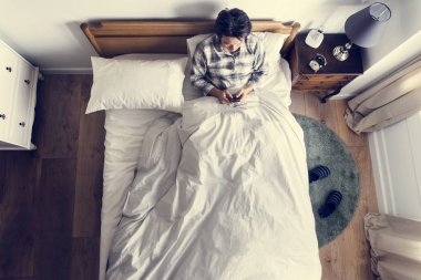 Telefonunuzun ve yatağa Asya etnik köken adam