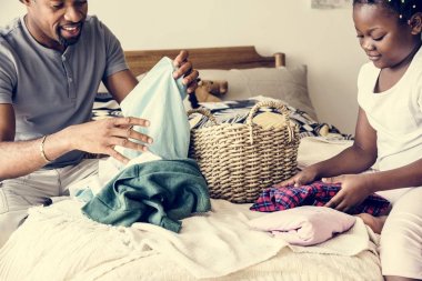 Dad and daughter folding clothes in bedroom together clipart