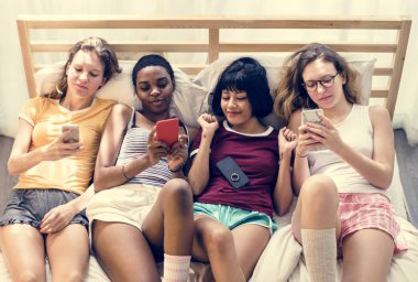 Çeşitli kadınların birlikte cep telefonunu kullanarak yatakta yatarken grup