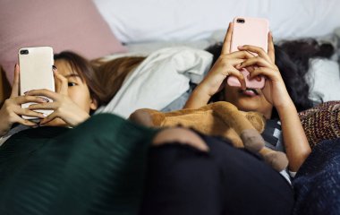 Genç kızların akıllı telefonlar bir yatağa kullanarak internet pijama partisi