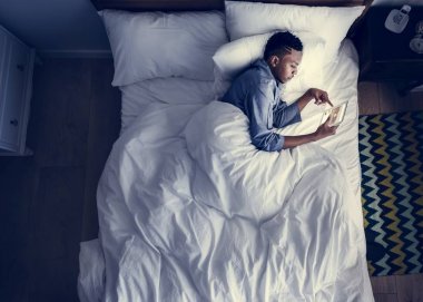 Karanlıkta bir dijital cihaz kullanarak yatakta adam