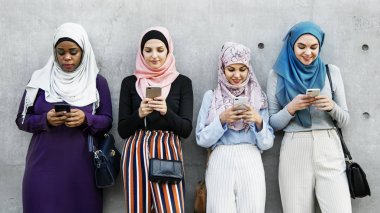 İslam kadın akıllı kullanarak grubu ayakta gri duvarının yakınında telefonları