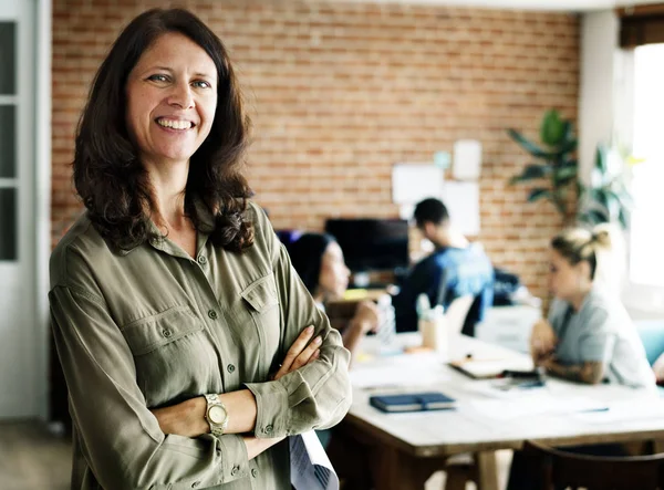 happy adult woman with crossed arms at startup office looking at camera