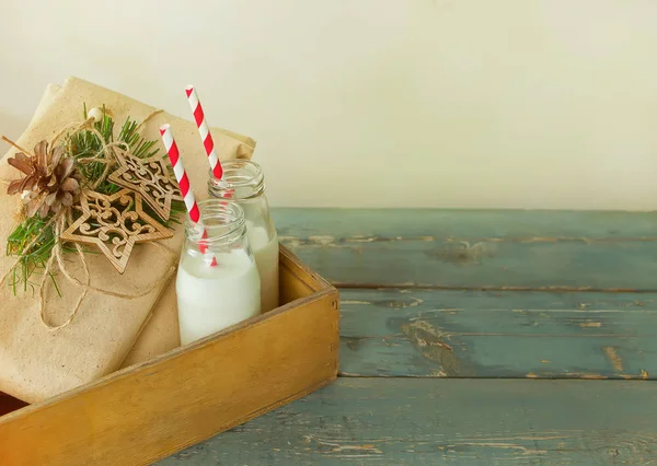 クリスマス プレゼント ミトン ボトルと木製のテーブルの上の小さなドーナツ牛乳 — ストック写真