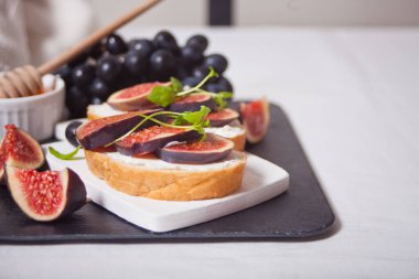 Krem peynirli sandviç, incir ve bal küçük beyaz bir kesme tahtasında servis ediliyor. Sağlıklı gıda konsepti