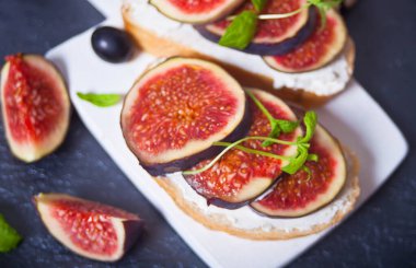 Krem peynirli sandviç, incir ve bal küçük beyaz bir kesme tahtasında servis ediliyor. Sağlıklı gıda konsepti