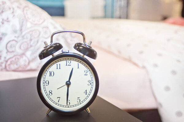 Будильник возле кровати дома. Утренняя концепция

