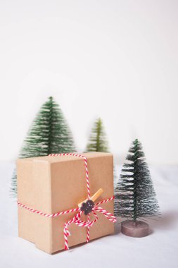 Mavi arka planda üç küçük Noel ağacı oyuncağıyla Noel hediyesi kutusu.