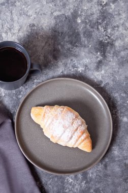 Gri tabakta taze kruvasan çörekleri ve yakınlarda bir fincan kahve..