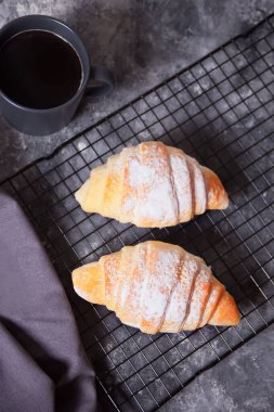 Taze kruvasan çörekleri fırın rafında ve yakınlarda bir fincan kahve.