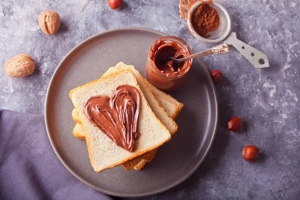 Torrada de pão com manteiga de creme de chocolate em forma de coração, frasco de creme de chocolate no fundo de concreto — Fotografia de Stock