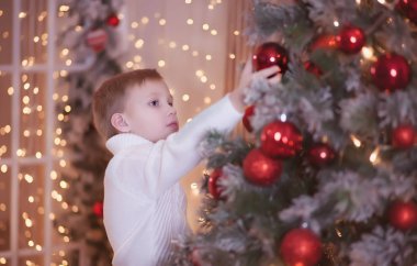 Beyaz süveterli bir çocuk Noel ağacı süslemiş..