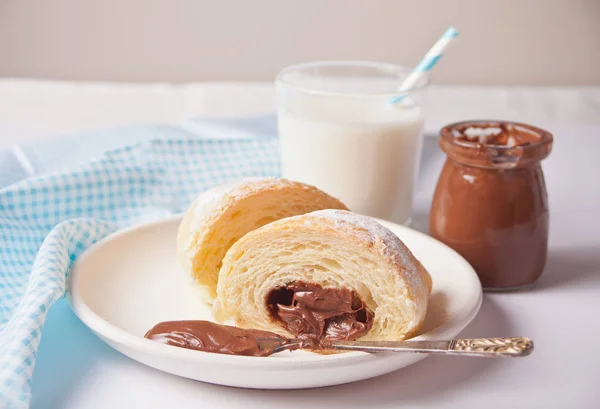Fresh croissants bun with chocolate on the plate, cup of coffee, jar of milk nearby on the white background — Stock Photo, Image