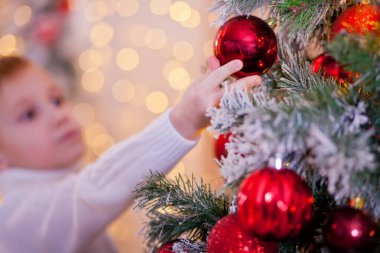 Beyaz süveterli bir çocuk Noel ağacı süslemiş..