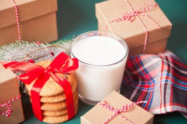 Bir bardak süt, kurabiye, Noel hediyesi kutuları ve yeşil masada çam dalı.