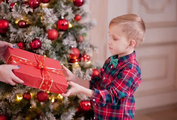 Женщина дать милый мальчик в клетчатой рубашке Рождество красный подарок коробку с елкой на заднем плане — стоковое фото