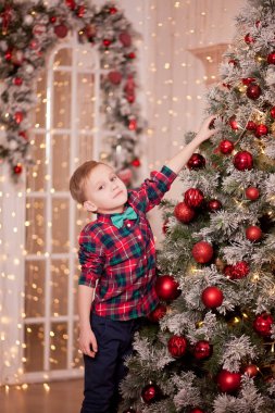 Beyaz süveterli bir çocuk Noel ağacı süslemiş..