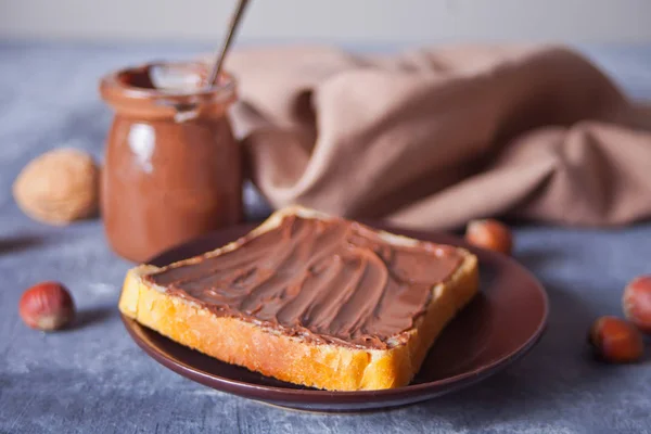 Хлеб тост с шоколадным сливочным маслом, банка шоколадного крема на бетонном фоне — стоковое фото