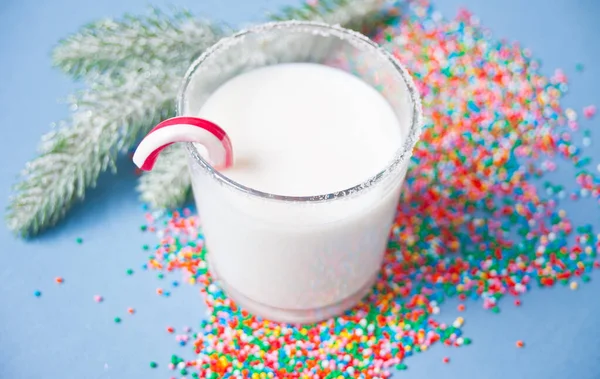 Glass of milk, candy cane, christmas tree branch on the blue background