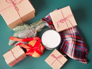 Bir bardak süt, kurabiye, hediye kutuları ve yeşil masada çam dalı. Noel konsepti.