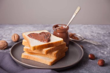 Kalp şeklinde çikolata kremalı ekmek tostu, beton arka planda çikolata kreması kavanozu.
