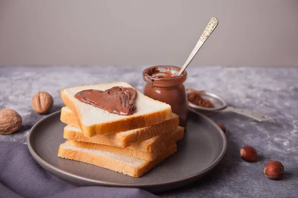 Хлебные тосты с шоколадным маслом в форме сердца, банка шоколадного крема на бетонном фоне — стоковое фото